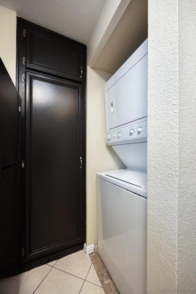 laundry room with light tile patterned floors, a textured ceiling, and stacked washing maching and dryer