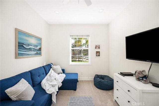 living area featuring light carpet, baseboards, and a ceiling fan