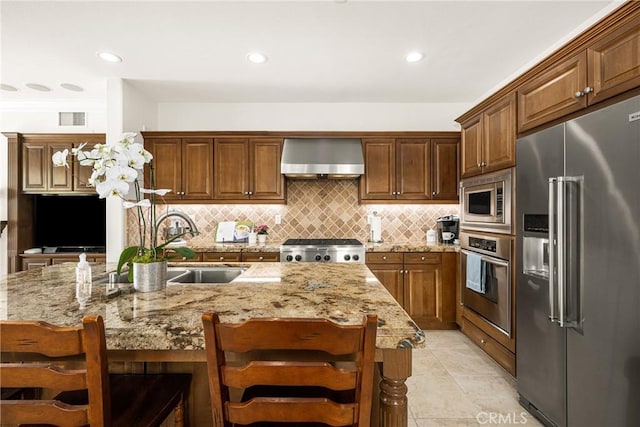 kitchen with stainless steel appliances, a breakfast bar, visible vents, wall chimney range hood, and a center island with sink