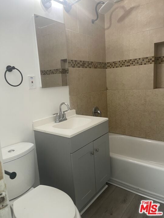 full bathroom featuring hardwood / wood-style flooring, vanity, tiled shower / bath combo, and toilet