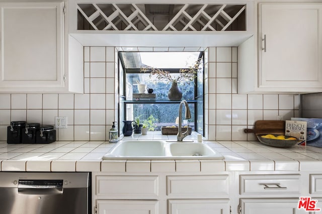 kitchen featuring white cabinetry, sink, backsplash, stainless steel dishwasher, and tile counters