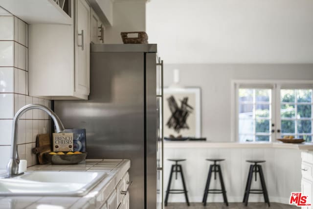 kitchen featuring tasteful backsplash, tile counters, sink, and white cabinets