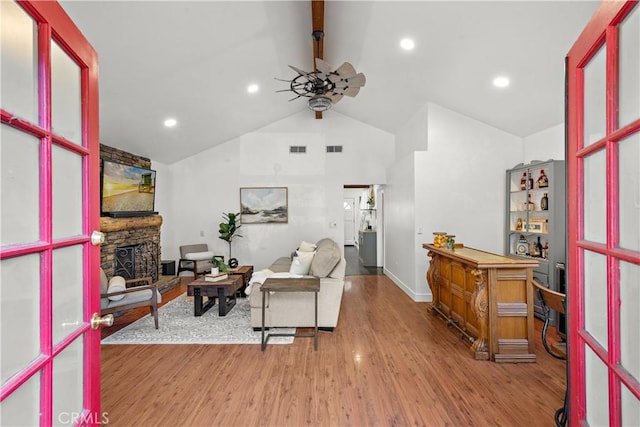 living room with ceiling fan, lofted ceiling, a stone fireplace, and hardwood / wood-style floors