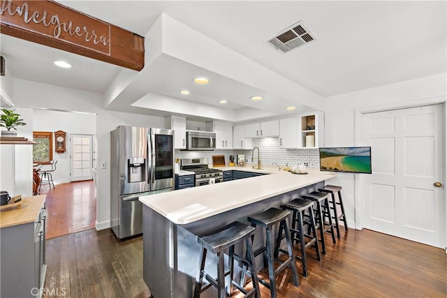 kitchen with stainless steel appliances, tasteful backsplash, white cabinets, a kitchen bar, and kitchen peninsula