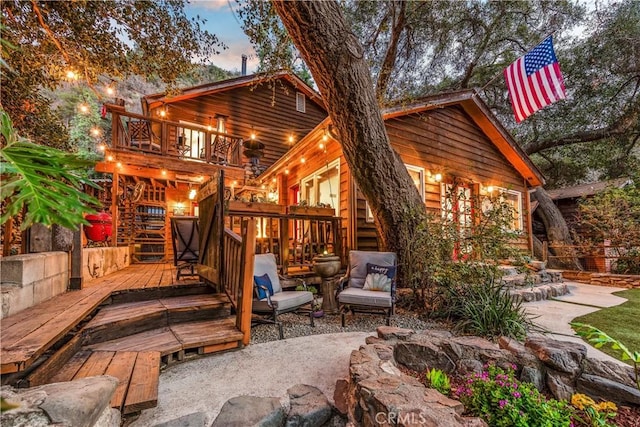 back house at dusk with a wooden deck, a balcony, and a patio