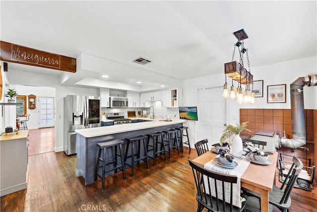 kitchen featuring pendant lighting, white cabinetry, stainless steel appliances, dark hardwood / wood-style flooring, and kitchen peninsula