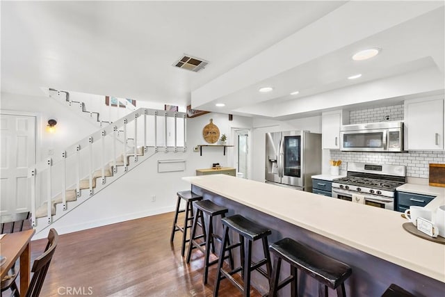 kitchen with dark wood-type flooring, a kitchen bar, white cabinetry, tasteful backsplash, and appliances with stainless steel finishes