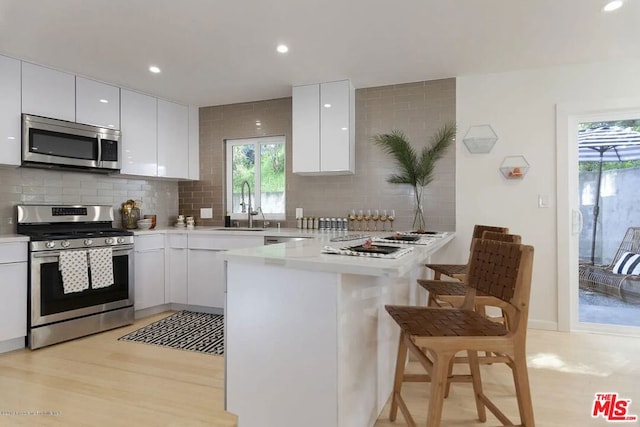 kitchen featuring appliances with stainless steel finishes, a kitchen bar, kitchen peninsula, and white cabinets