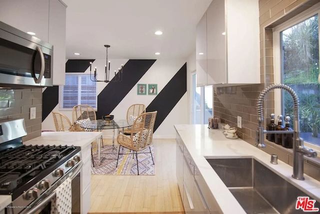 kitchen with sink, decorative light fixtures, stainless steel appliances, light hardwood / wood-style floors, and white cabinets