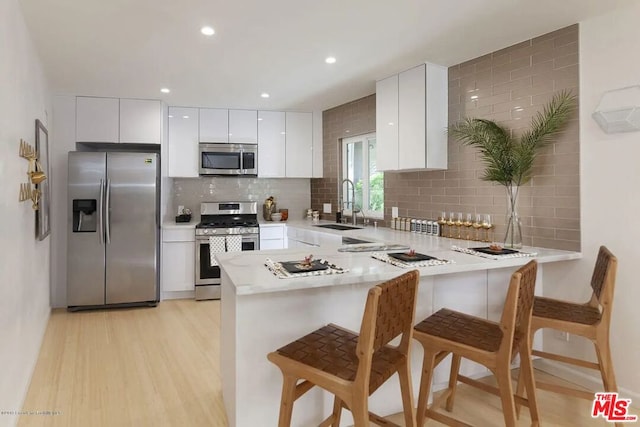 kitchen featuring sink, white cabinets, a kitchen breakfast bar, kitchen peninsula, and stainless steel appliances