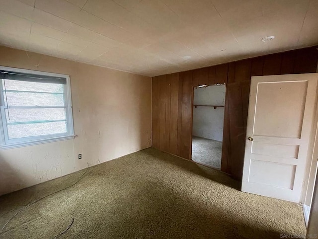 unfurnished bedroom with a closet, carpet floors, and wood walls