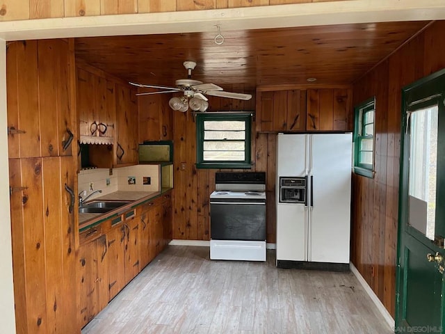 kitchen featuring wooden walls, sink, ceiling fan, white appliances, and light hardwood / wood-style flooring