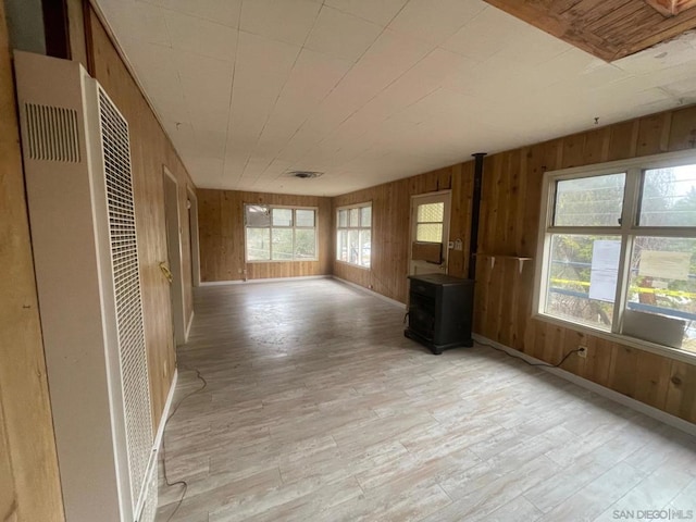 unfurnished living room with light wood-type flooring, wood walls, and a wood stove