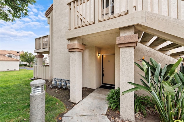 view of exterior entry featuring a yard and a balcony