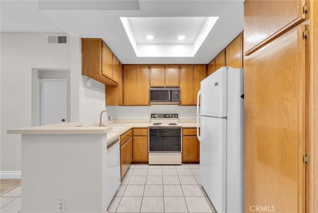 kitchen featuring sink, light tile patterned floors, a tray ceiling, kitchen peninsula, and white appliances