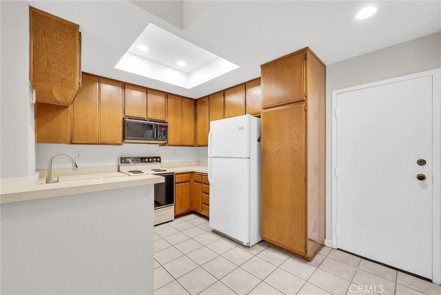 kitchen with a tray ceiling, sink, white appliances, and light tile patterned flooring