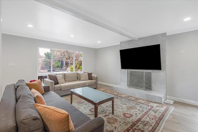 living room with a fireplace, ornamental molding, beam ceiling, and light hardwood / wood-style floors