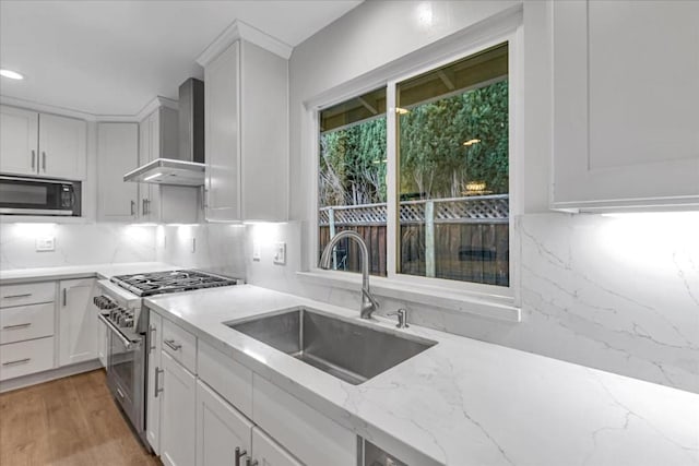 kitchen with wall chimney exhaust hood, sink, white cabinetry, stainless steel stove, and light stone countertops