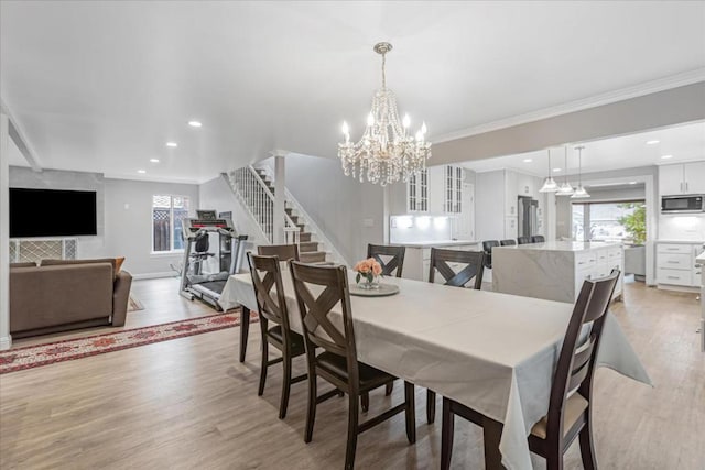 dining space with a notable chandelier, ornamental molding, and light wood-type flooring