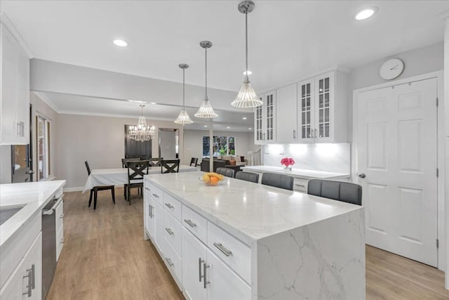 kitchen with a center island, light wood-type flooring, pendant lighting, light stone countertops, and white cabinets