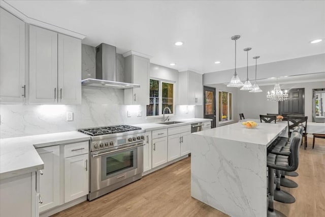 kitchen featuring wall chimney range hood, white cabinetry, stainless steel appliances, a center island, and light stone countertops