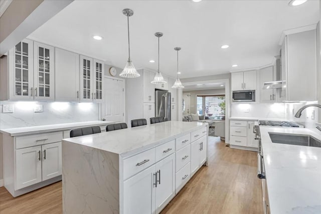 kitchen featuring pendant lighting, appliances with stainless steel finishes, white cabinetry, light stone counters, and a kitchen island