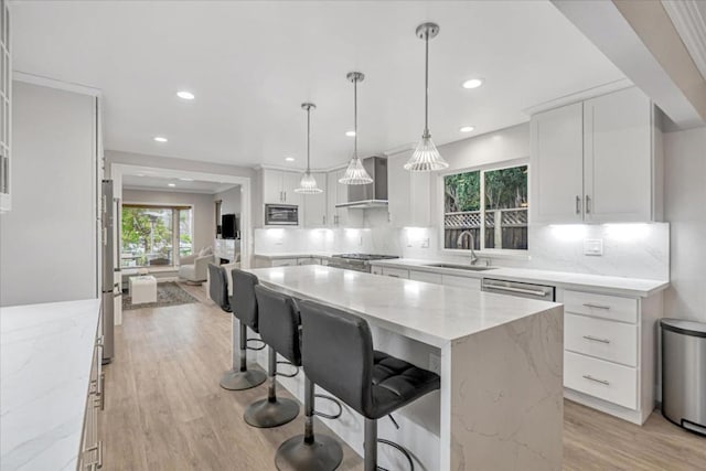 kitchen featuring light stone counters, wall chimney exhaust hood, a kitchen island, and white cabinets