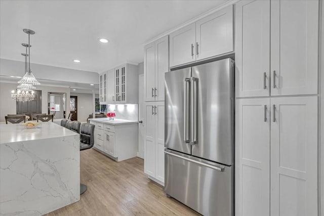 kitchen with white cabinetry, high end refrigerator, hanging light fixtures, light hardwood / wood-style floors, and light stone countertops