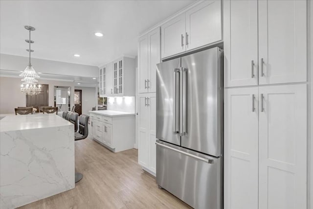 kitchen featuring pendant lighting, white cabinetry, light stone countertops, high quality fridge, and light wood-type flooring