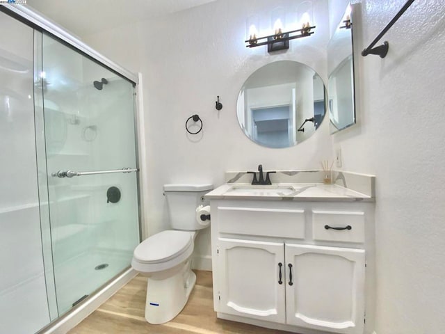 bathroom featuring a shower with door, vanity, hardwood / wood-style floors, and toilet