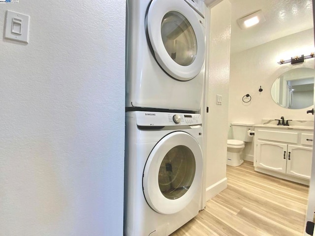 laundry area with stacked washer and clothes dryer, sink, and light hardwood / wood-style flooring