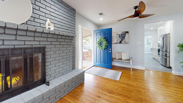 foyer entrance with ceiling fan, a fireplace, and light wood-type flooring