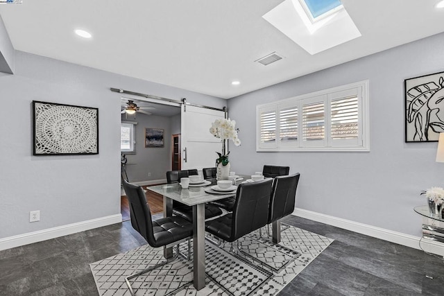 dining space featuring ceiling fan, a barn door, and a skylight