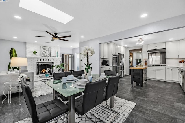 dining room with a skylight, a fireplace, and ceiling fan