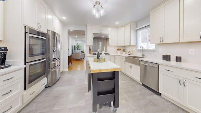 kitchen with sink, butcher block countertops, appliances with stainless steel finishes, white cabinetry, and a center island