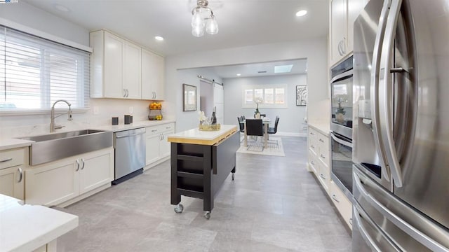 kitchen with sink, white cabinets, stainless steel appliances, a barn door, and a healthy amount of sunlight