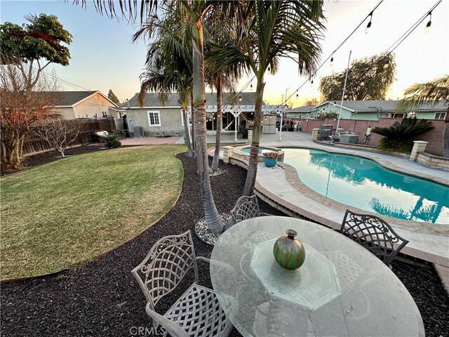 pool at dusk featuring a jacuzzi, a patio area, and a lawn