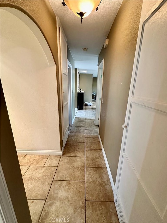 hallway with a textured ceiling and light tile patterned floors