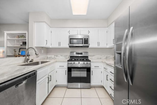 kitchen with appliances with stainless steel finishes, light tile patterned flooring, white cabinetry, a sink, and light stone countertops