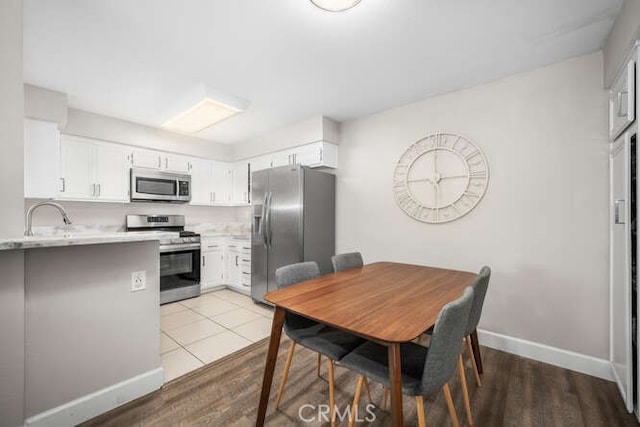 kitchen with stainless steel appliances, light countertops, white cabinetry, a sink, and baseboards