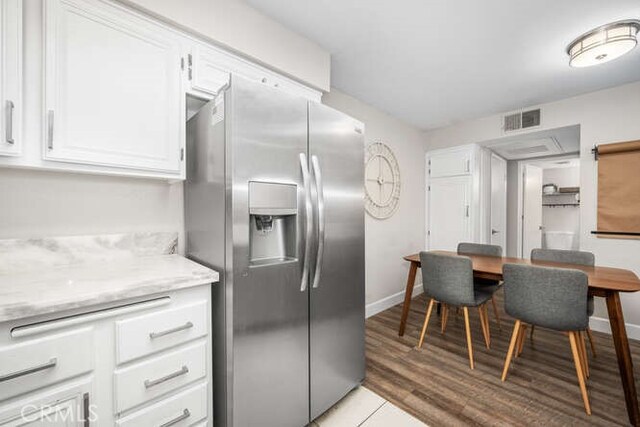 kitchen featuring white cabinetry, light stone counters, light hardwood / wood-style flooring, and stainless steel refrigerator with ice dispenser