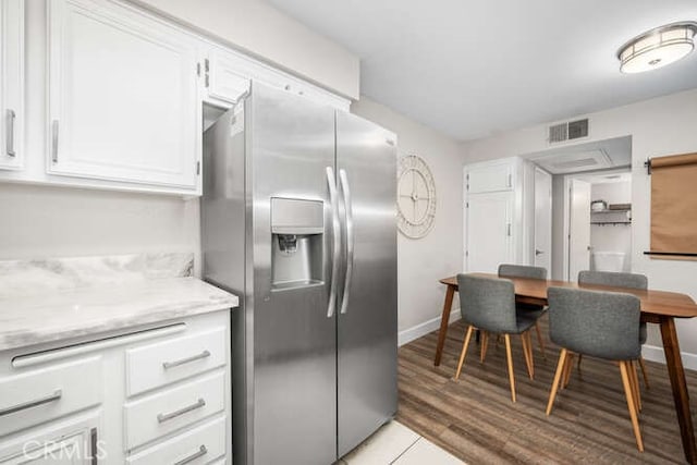 kitchen featuring stainless steel refrigerator with ice dispenser, visible vents, light wood-style floors, white cabinets, and light stone countertops