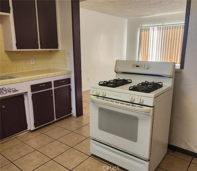116 Beardsley Ave, Bakersfield, CA 93308 - kitchen with white gas range oven, tile counters, tasteful backsplash, light tile patterned floors, and a textured ceiling