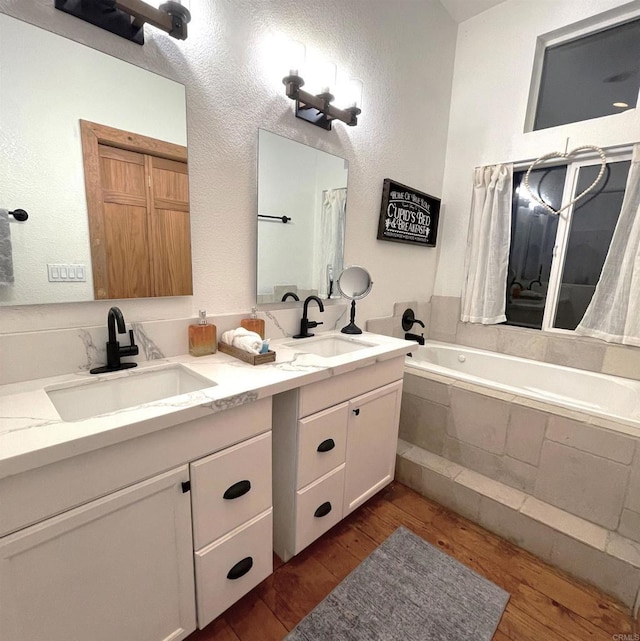 bathroom with wood-type flooring, tiled bath, and vanity