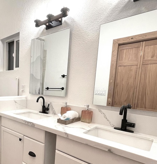 full bathroom with a textured wall, a sink, and double vanity