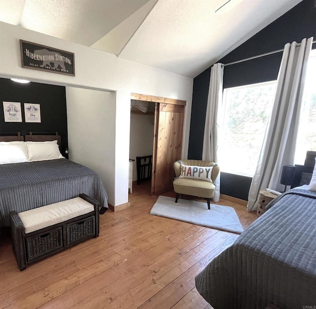 bedroom featuring light wood-style floors, vaulted ceiling, a textured ceiling, and baseboards