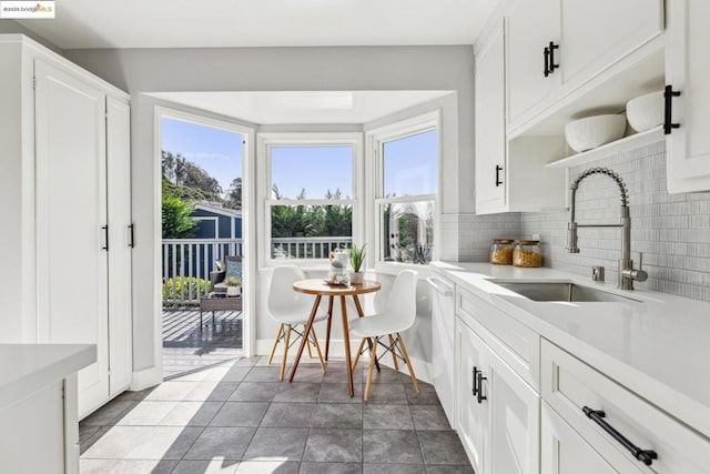 kitchen with dishwasher, sink, dark tile patterned flooring, white cabinets, and decorative backsplash