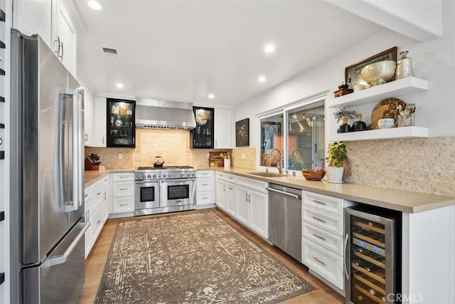 kitchen featuring white cabinetry, sink, wine cooler, high end appliances, and wall chimney exhaust hood