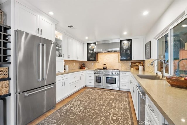 kitchen featuring sink, white cabinets, wall chimney exhaust hood, and high quality appliances