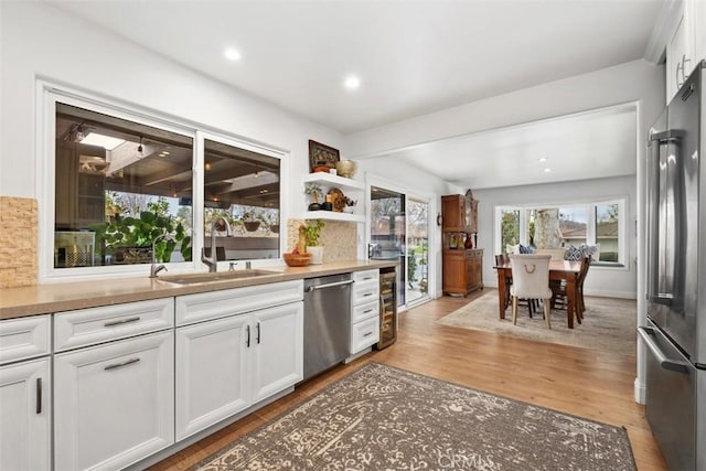 kitchen featuring white cabinetry, sink, backsplash, light hardwood / wood-style floors, and stainless steel appliances